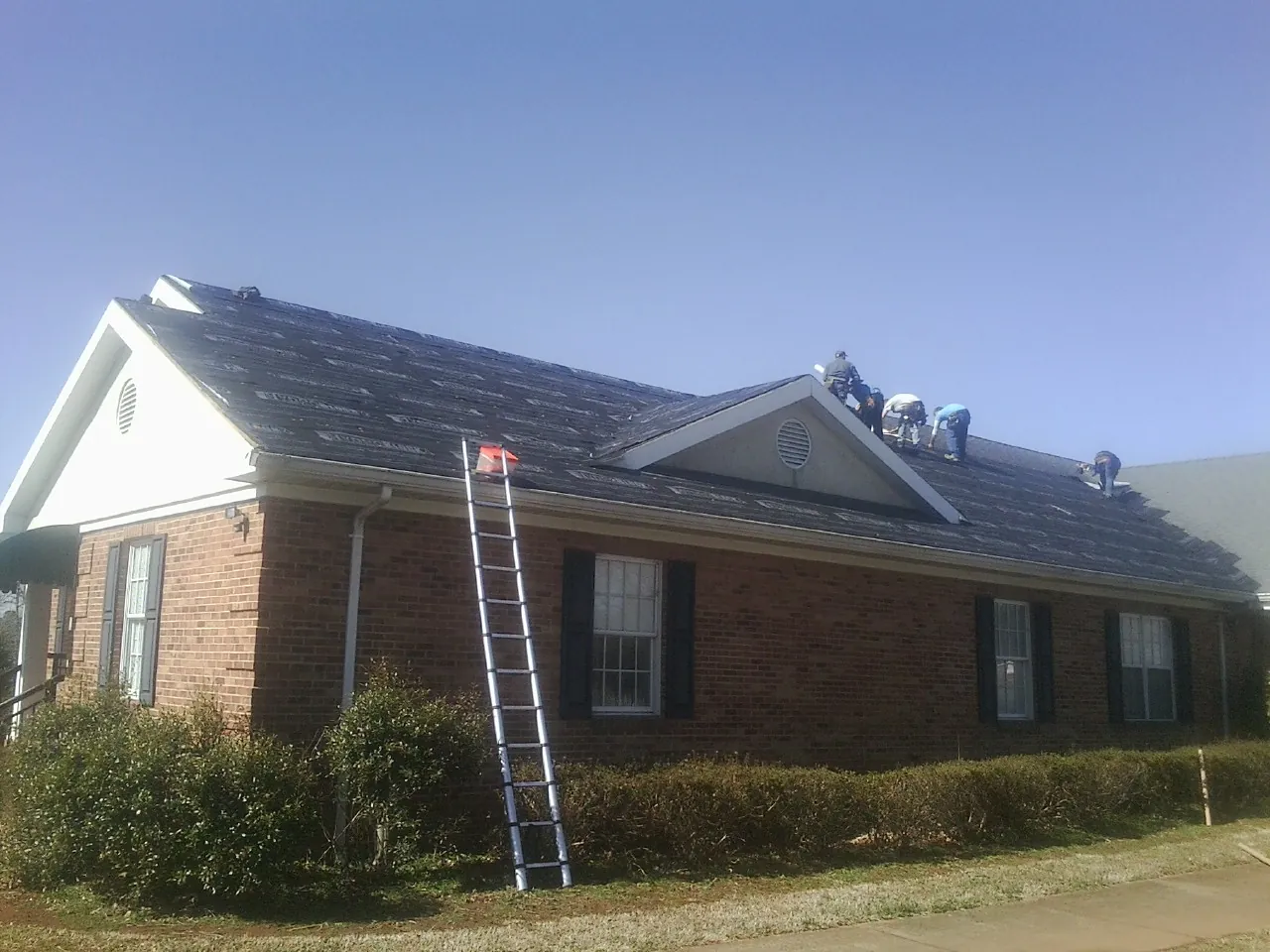 Crew tearing shingles off a brick ranch roof with a ladder set — Emergency Roof Repair work by our crew in Thomson