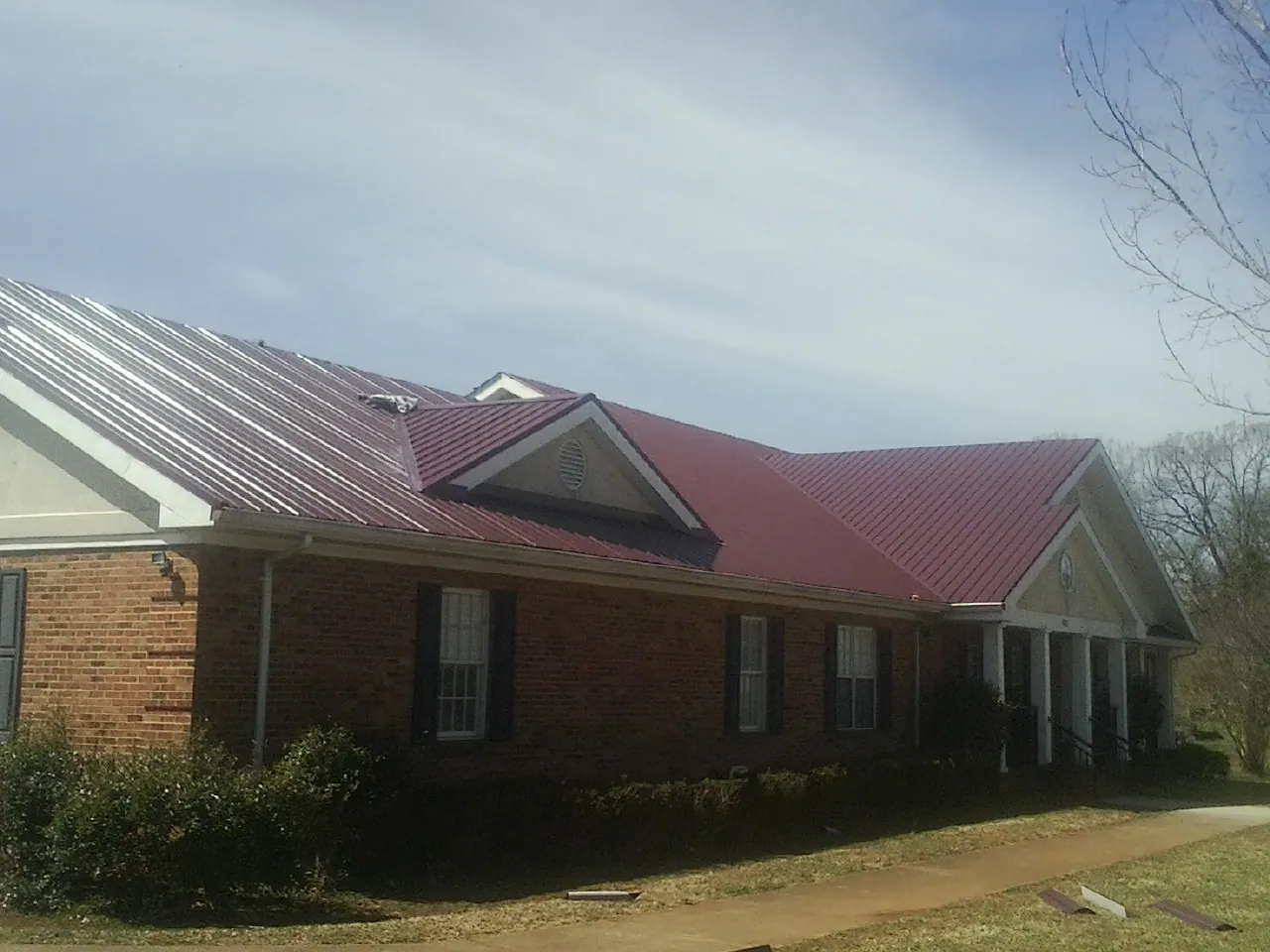 Red metal roof with gabled entries on a long brick building, from a Hail Damage Roof Repair job in Thomson