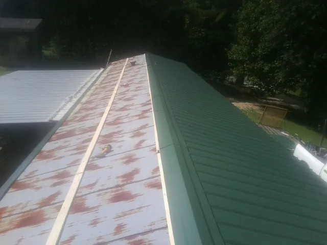 Old rusted panels beside newly installed green metal roofing — Wind Damage Roof Repair by Roofing Brothers in Thomson