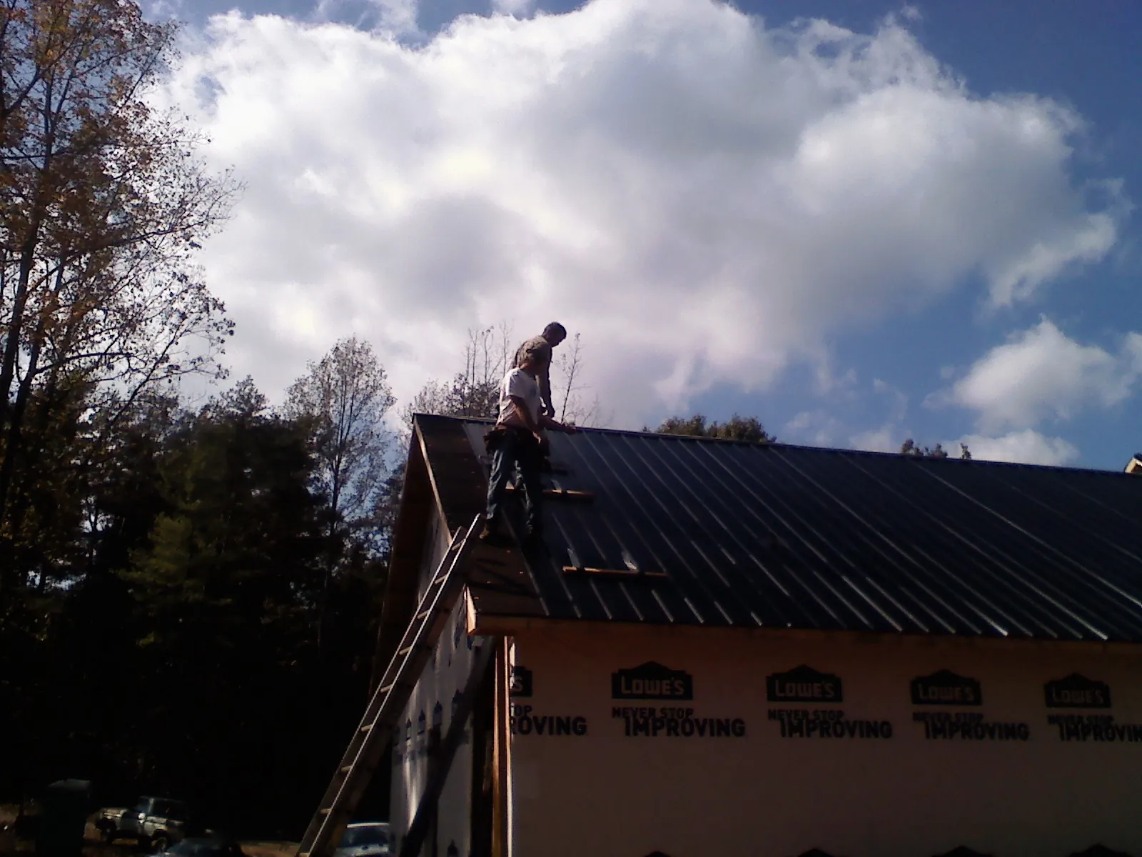 Roofer fastening dark metal panels high against a cloudy sky, from a Roof Inspection job in Thomson